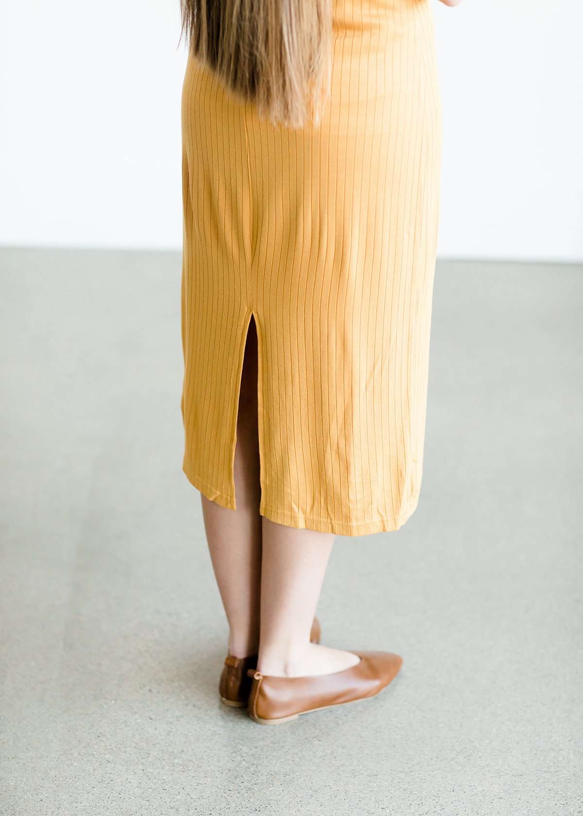 Woman wearing a ribbed mustard midi dress with faux wood buttons.