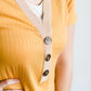 Woman wearing a ribbed mustard midi dress with faux wood buttons.