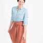 Woman wearing a button front self tie pink midi skirt with big pockets and paired with dress heels and chambray top