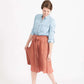 Woman wearing a button front self tie pink midi skirt with big pockets and paired with dress heels and chambray top