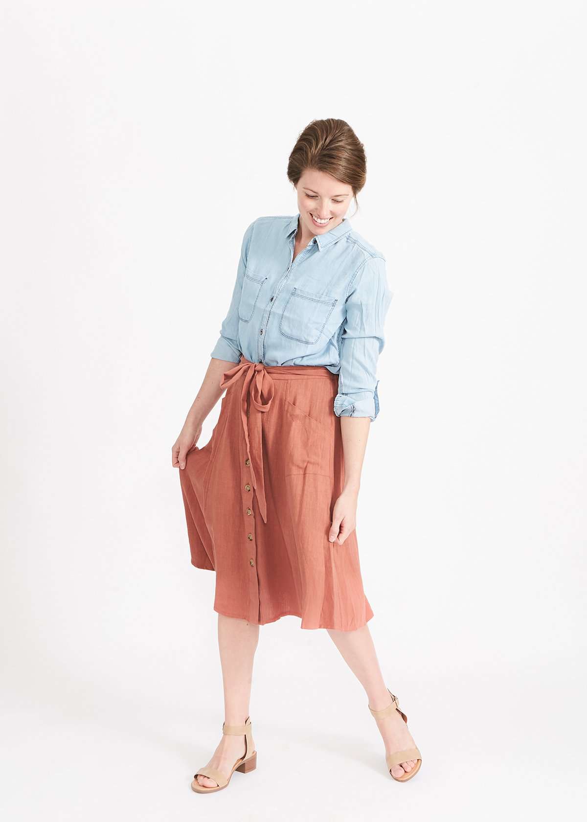 Woman wearing a button front self tie pink midi skirt with big pockets and paired with dress heels and chambray top