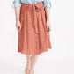 Woman wearing a button front self tie pink midi skirt with big pockets and paired with dress heels and chambray top