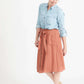 Woman wearing a button front self tie pink midi skirt with big pockets and paired with dress heels and chambray top