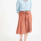 Woman wearing a button front self tie pink midi skirt with big pockets and paired with dress heels and chambray top