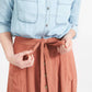 Woman wearing a button front self tie pink midi skirt with big pockets and paired with dress heels and chambray top