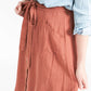 Woman wearing a button front self tie pink midi skirt with big pockets and paired with dress heels and chambray top