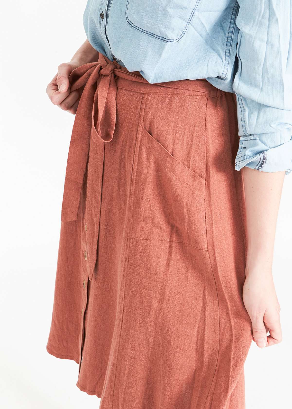 Woman wearing a button front self tie pink midi skirt with big pockets and paired with dress heels and chambray top