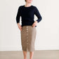 Woman wearing a khaki midi length skirt with faux buttons running down the front. It is paired with a navy sweater and copper, suede slide shoes.