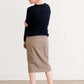 Woman wearing a khaki midi length skirt with faux buttons running down the front. It is paired with a navy sweater and copper, suede slide shoes.