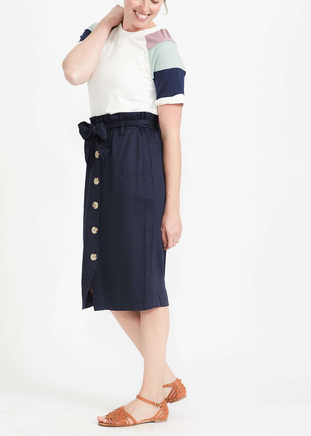 Woman wearing a navy button front paper bag style midi skirt.