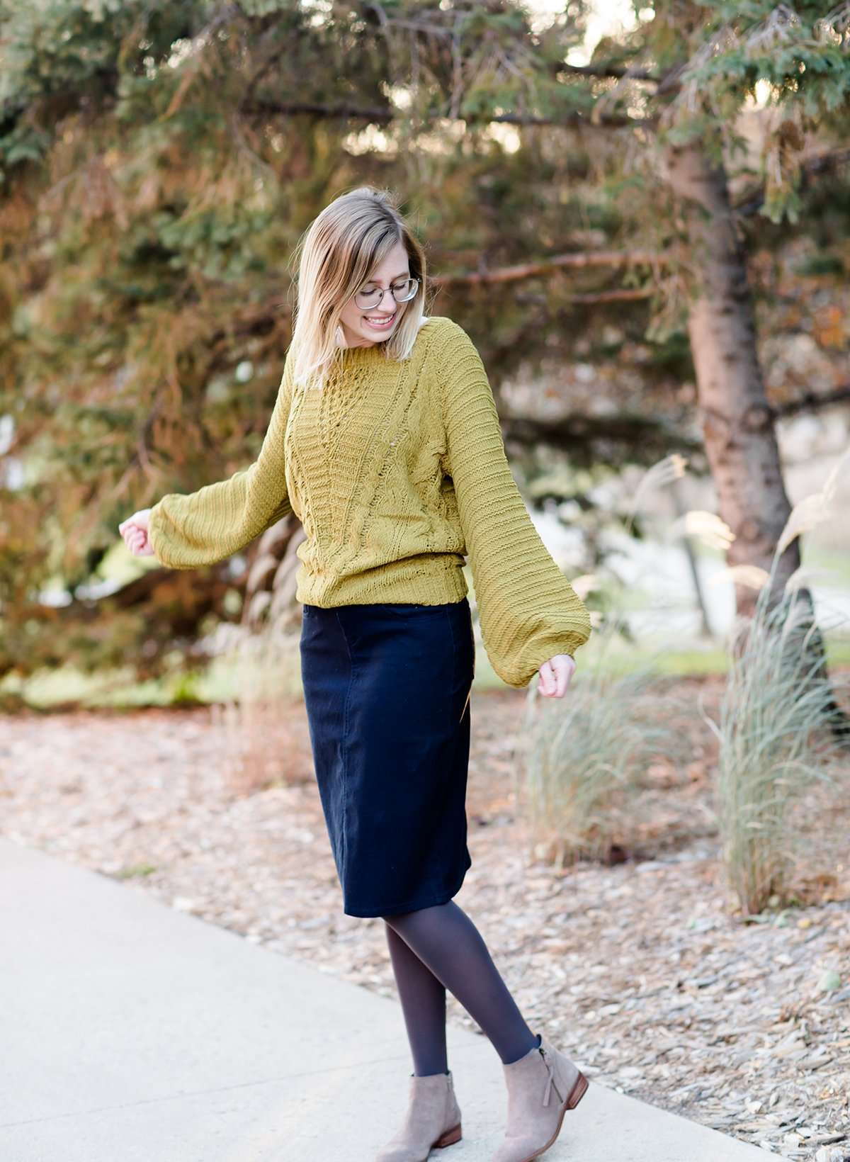 Young woman wearing a balloon sleeve chenille-like sweater with a below the knee navy midi skirt
