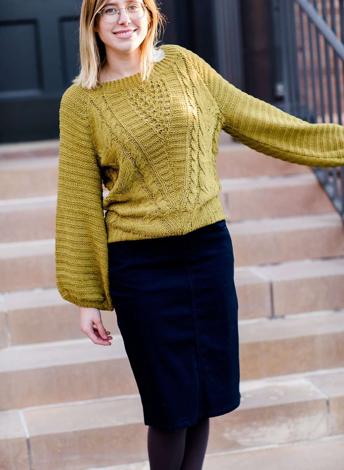 Young woman wearing a balloon sleeve chenille like sweater with a below the knee navy midi skirt