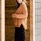 Woman wearing an open front cardigan that is chenille and camel in color. She is also wearing it over a black dress and brown riding boots. She is standing on the stairs at Inherit Clothing Company.