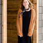 Woman wearing an open front cardigan that is chenille and camel in color. She is also wearing it over a black dress and brown riding boots. She is standing on the stairs at Inherit Clothing Company.