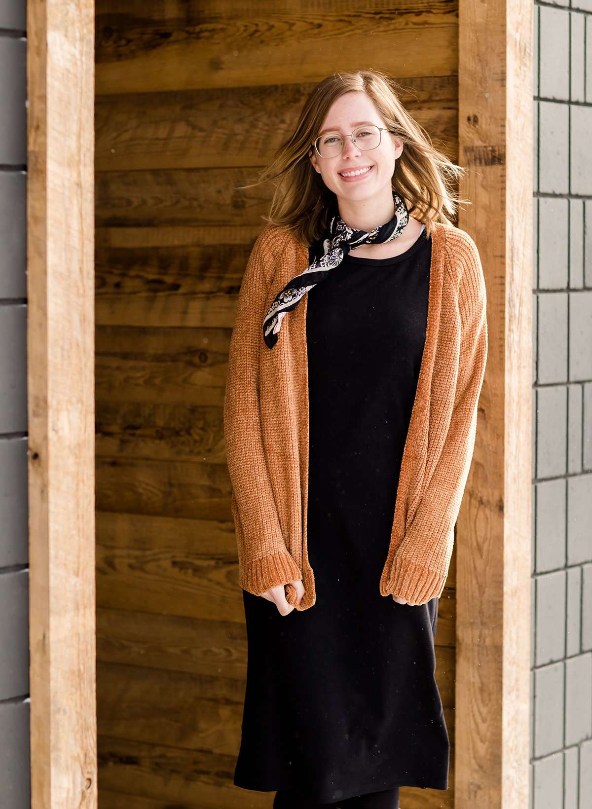 Woman wearing an open front cardigan that is chenille and camel in color. She is also wearing it over a black dress and brown riding boots. She is standing on the stairs at Inherit Clothing Company.