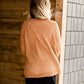 Woman wearing an open front cardigan that is chenille and camel in color. She is also wearing it over a black dress and brown riding boots. She is standing on the stairs at Inherit Clothing Company.