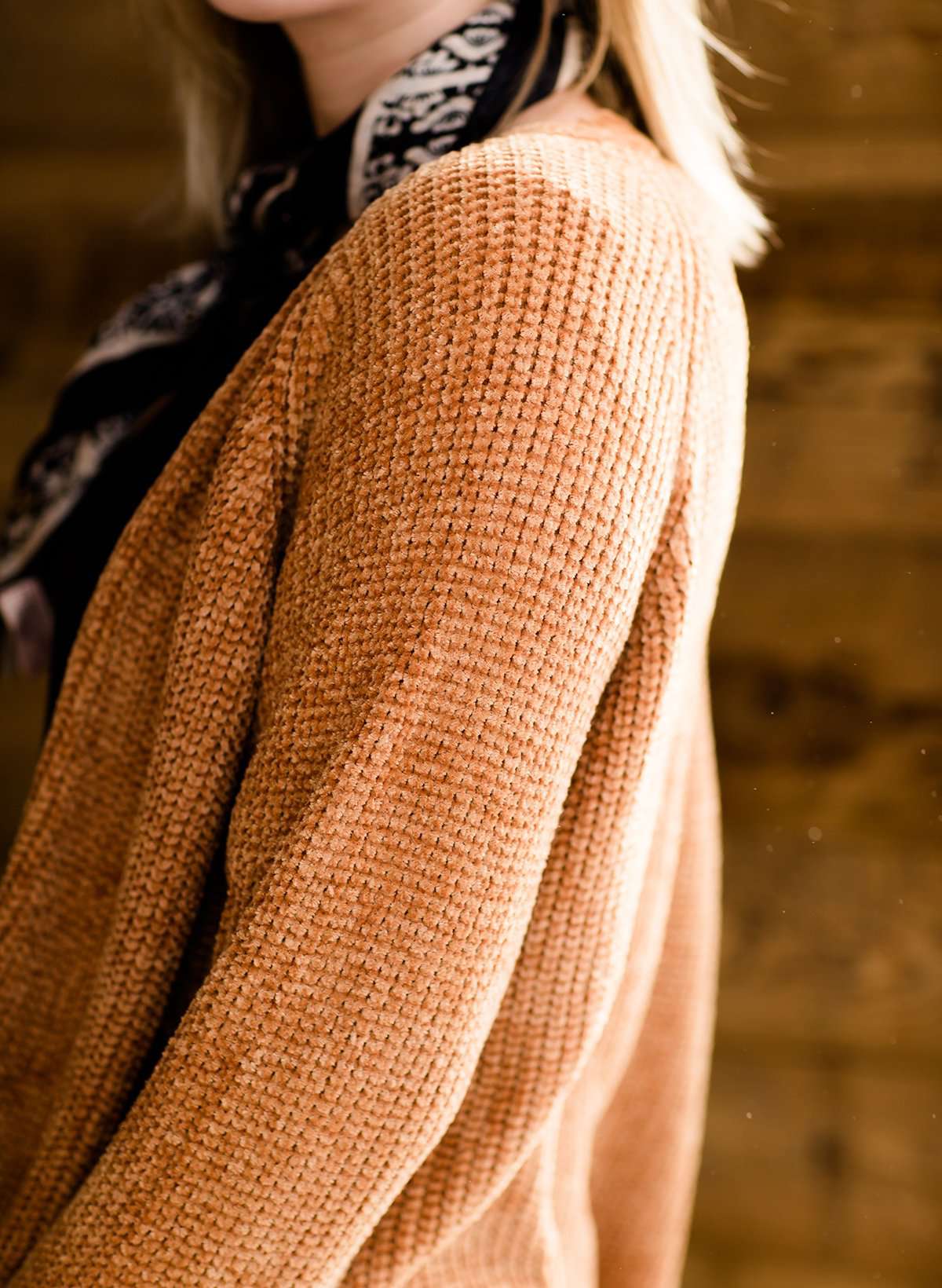 Woman wearing an open front cardigan that is chenille and camel in color. She is also wearing it over a black dress and brown riding boots. She is standing on the stairs at Inherit Clothing Company.