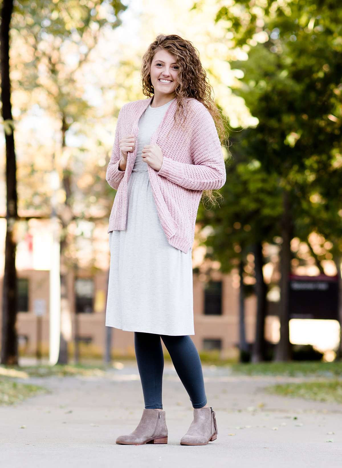 Woman wearing a pink shrug chenille sweater with open front and extra length in the back.