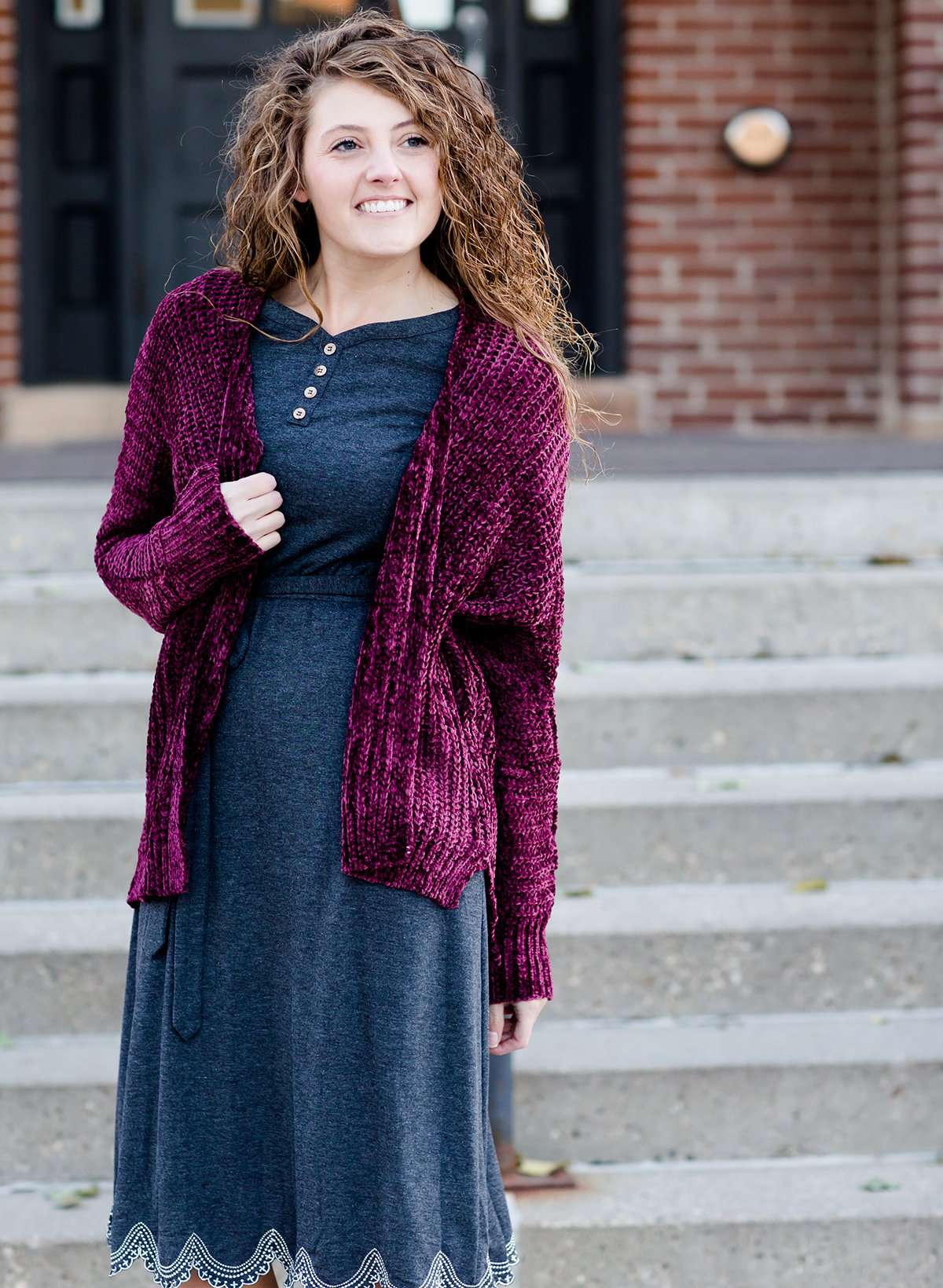 Woman wearing a wine colored shrug chenille sweater with open front and extra length in the back.