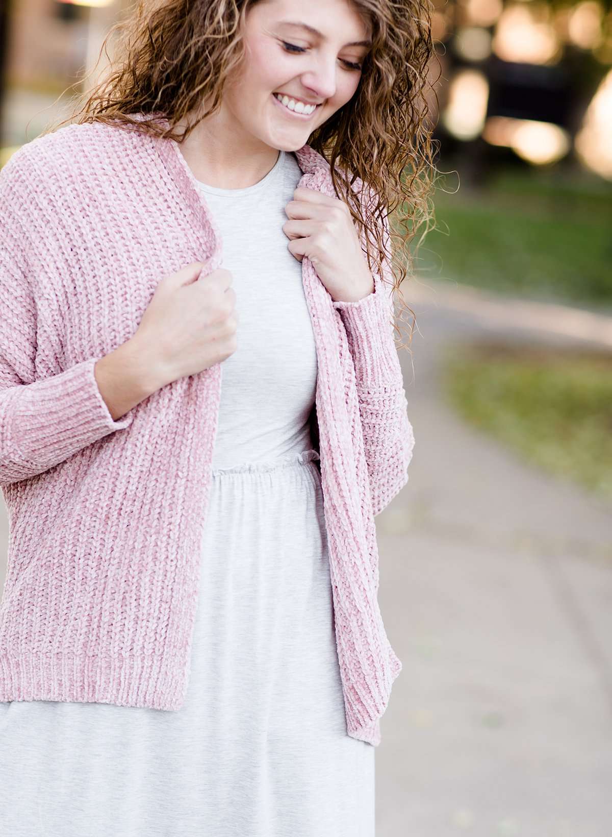 Woman wearing a pink shrug chenille sweater with open front and extra length in the back.