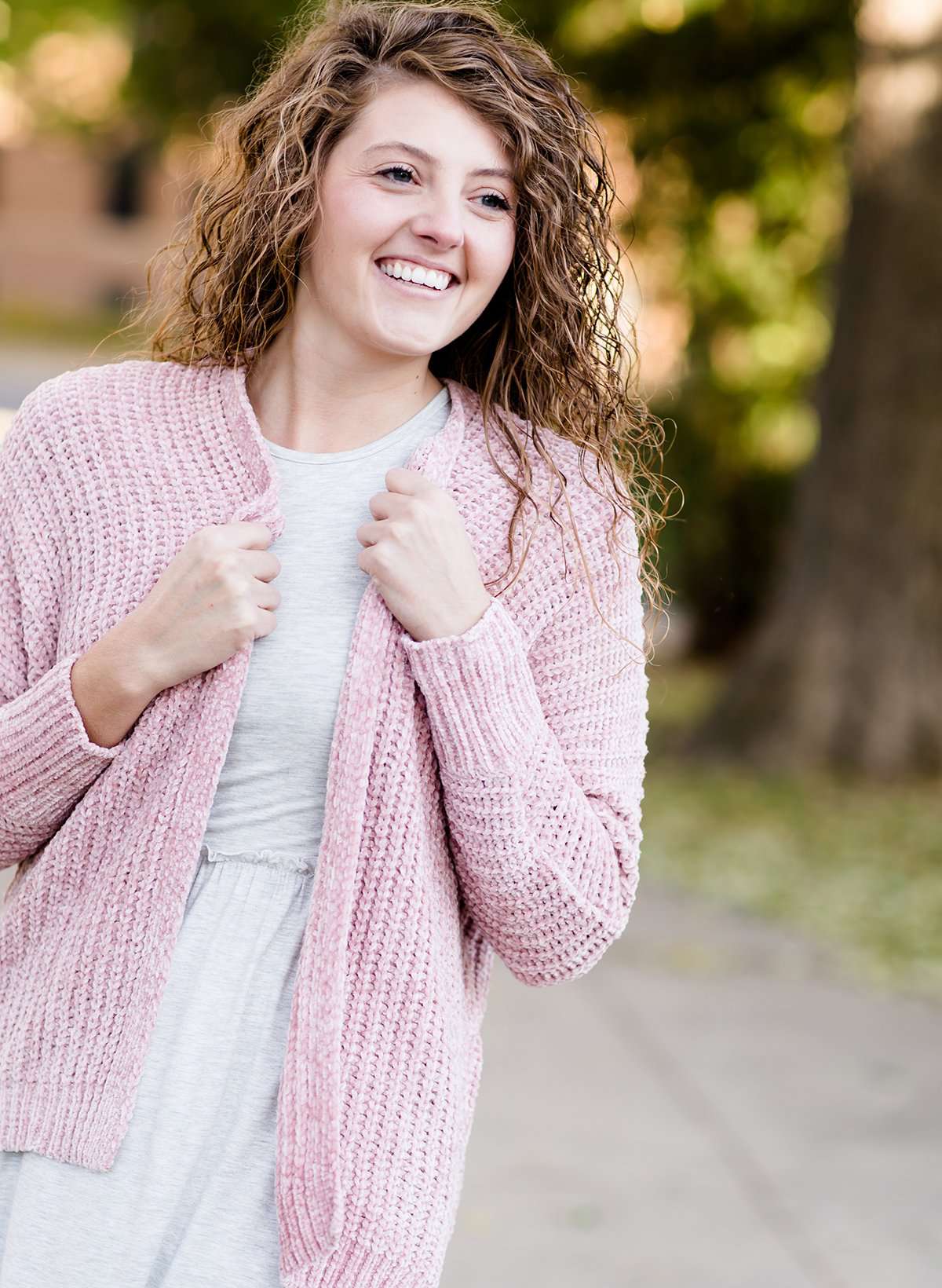 Woman wearing a pink shrug chenille sweater with open front and extra length in the back.