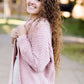 Woman wearing a pink shrug chenille sweater with open front and extra length in the back.