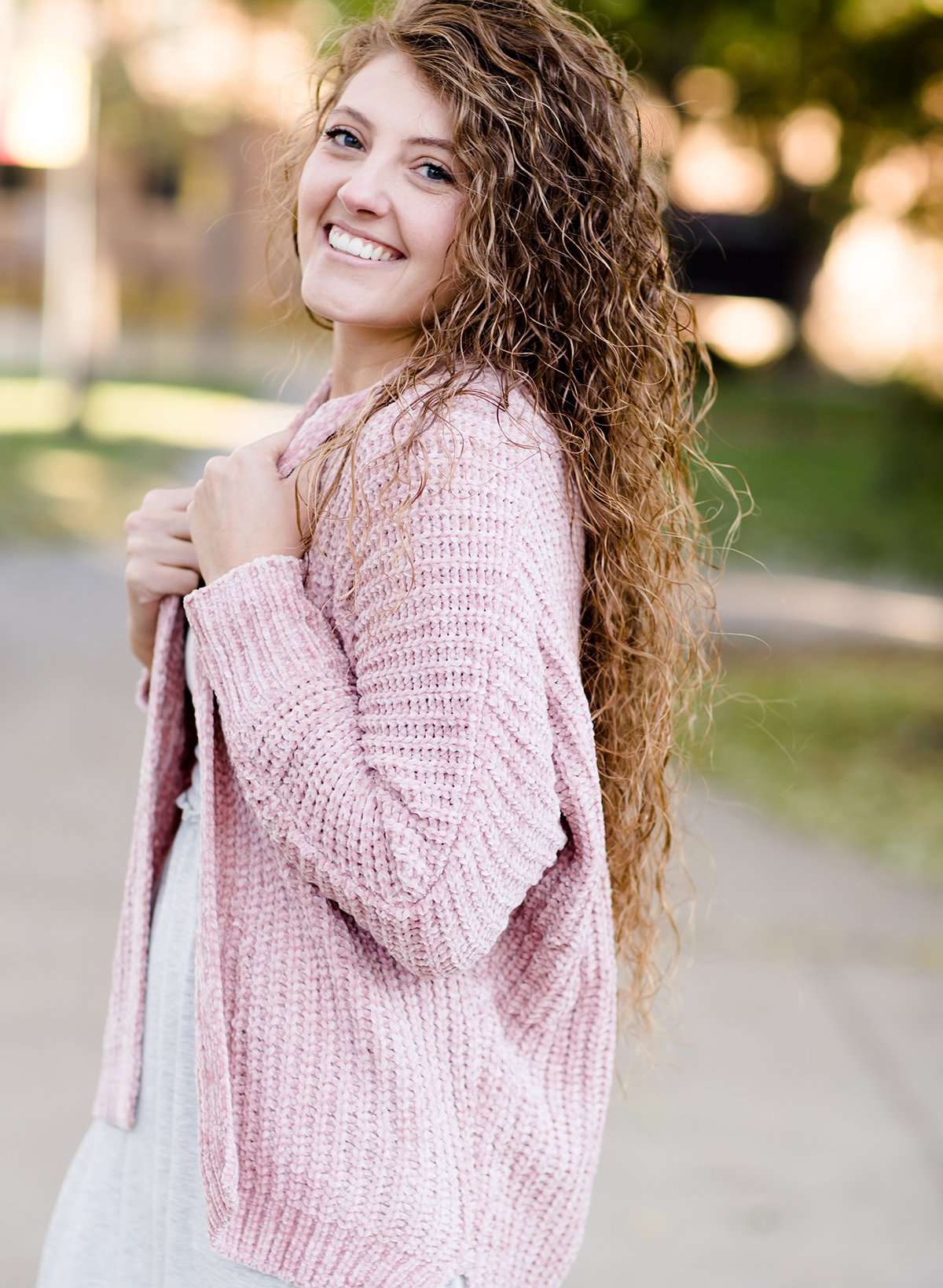 Woman wearing a pink shrug chenille sweater with open front and extra length in the back.