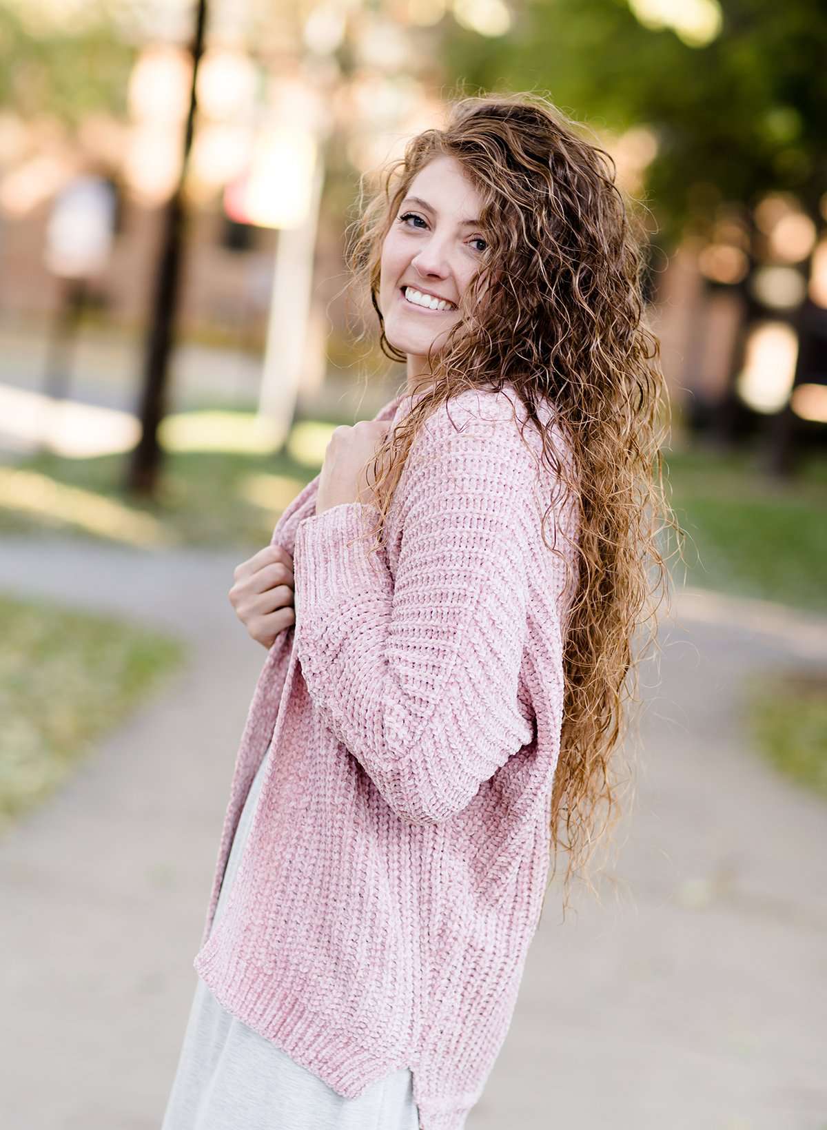 Woman wearing a pink shrug chenille sweater with open front and extra length in the back.