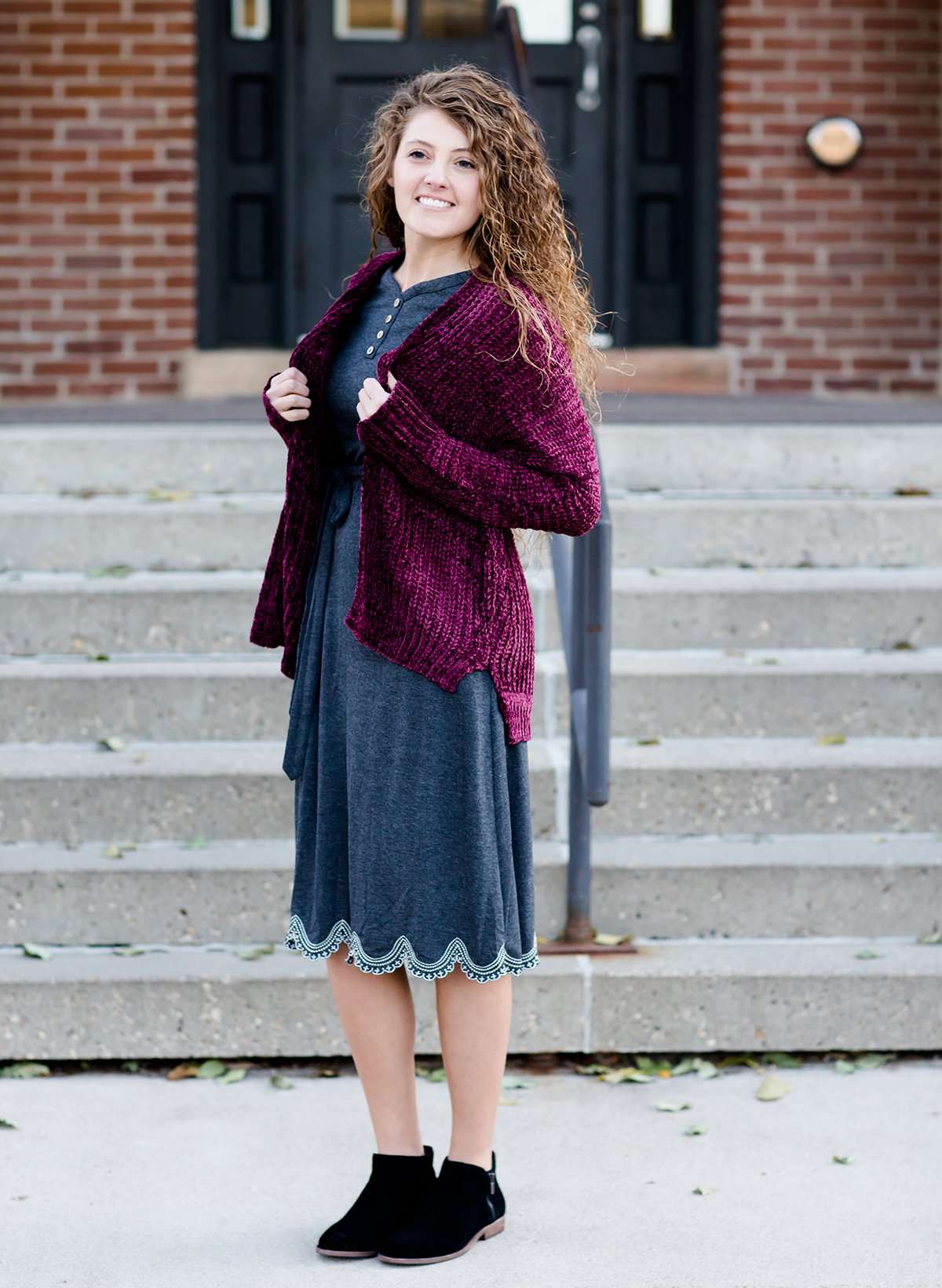 Woman wearing a wine colored shrug chenille sweater with open front and extra length in the back.