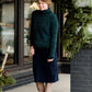 Woman wearing a dark green chenille turtle neck paired with a modest black midi skirt standing outside of Inherit Clothing Company