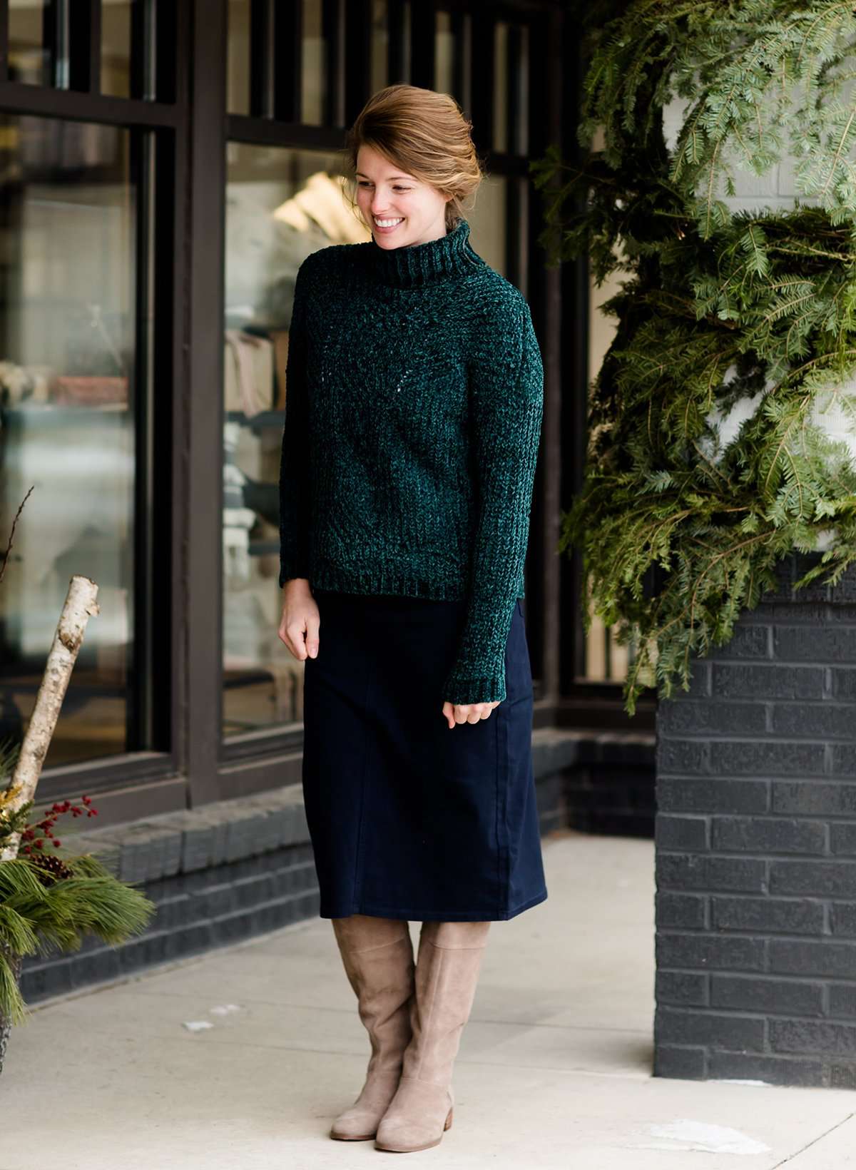 Woman wearing a dark green chenille turtle neck paired with a modest black midi skirt standing outside of Inherit Clothing Company