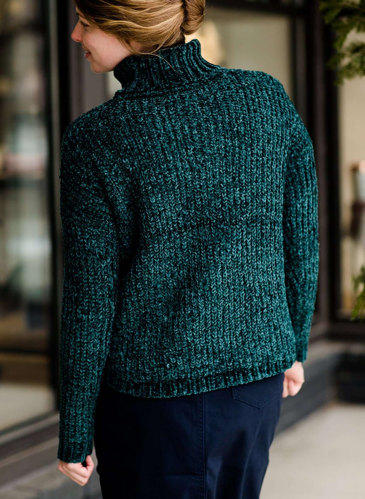 Woman wearing a dark green chenille turtle neck paired with a modest black midi skirt standing outside of Inherit Clothing Company