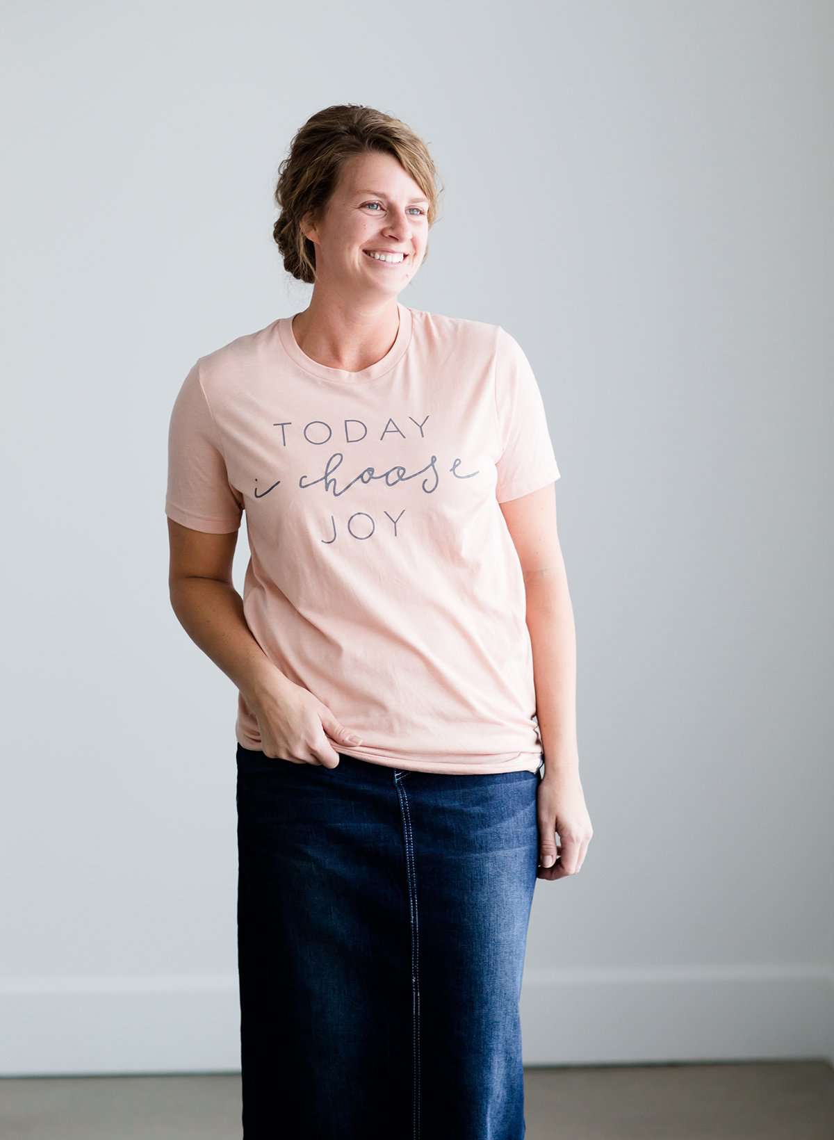 Woman wearing a blush colored modest graphic tee that says, Today I Choose Joy. This tee is a triblend of material and is paired with a long denim modest skirt and chambray top.