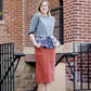Woman wearing a below the knee corduroy skirt. This skirt is a fin corduroy with a gold button snap, no slit and no back pockets. It comes in burgundy, teal, burnt orange and dark khaki.