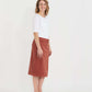 Woman wearing a below the knee corduroy skirt. This skirt is a fin corduroy with a gold button snap, no slit and no back pockets. It comes in burgundy, teal, burnt orange and dark khaki.