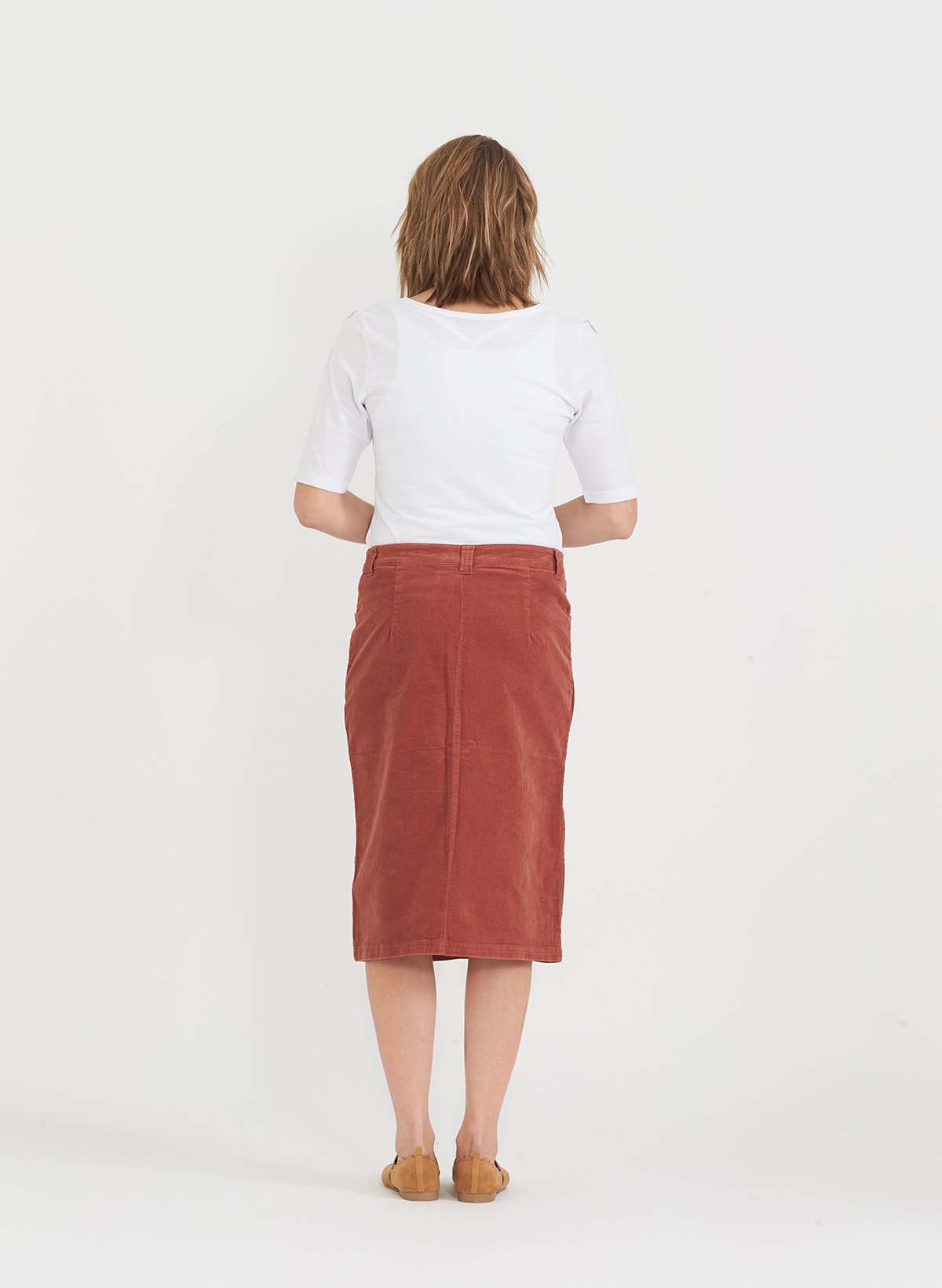 Woman wearing a below the knee corduroy skirt. This skirt is a fin corduroy with a gold button snap, no slit and no back pockets. It comes in burgundy, teal, burnt orange and dark khaki.