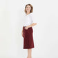 Woman wearing a below the knee corduroy skirt. This skirt is a fin corduroy with a gold button snap, no slit and no back pockets. It comes in burgundy, teal, burnt orange and dark khaki.