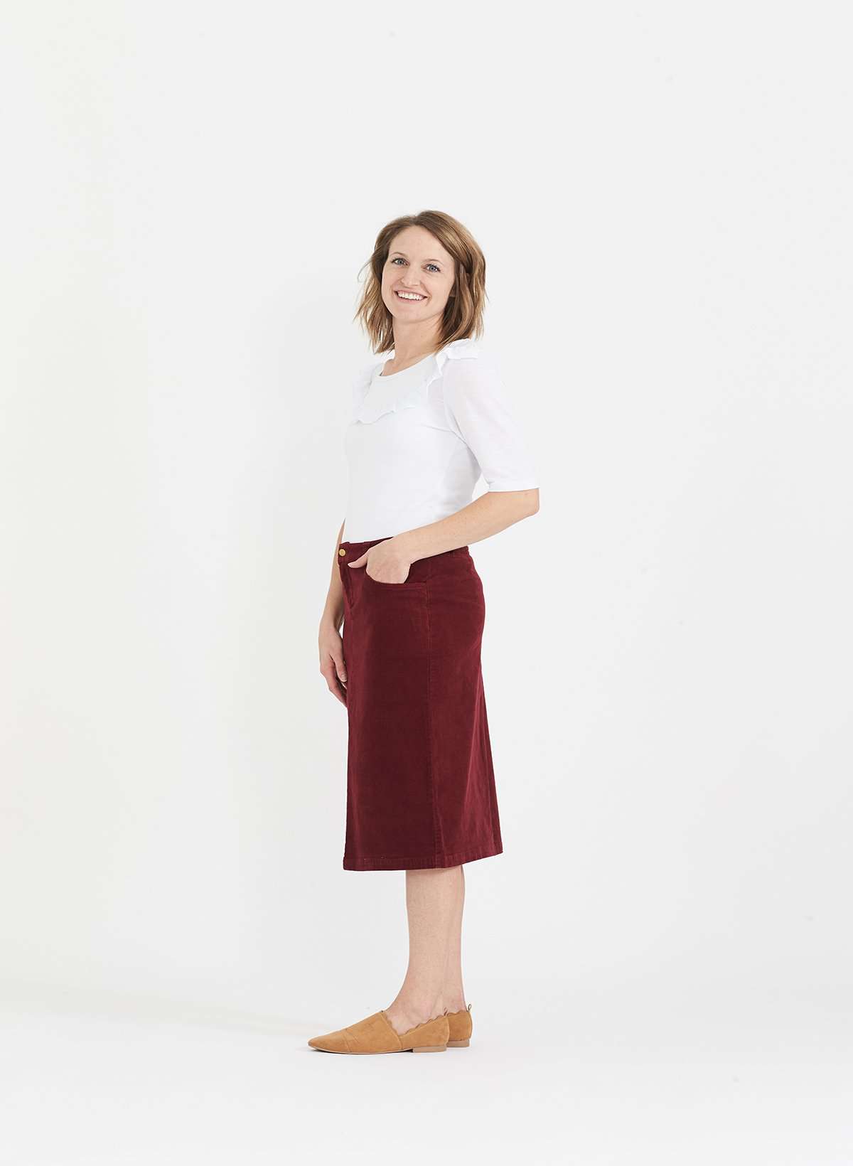 Woman wearing a below the knee corduroy skirt. This skirt is a fin corduroy with a gold button snap, no slit and no back pockets. It comes in burgundy, teal, burnt orange and dark khaki.