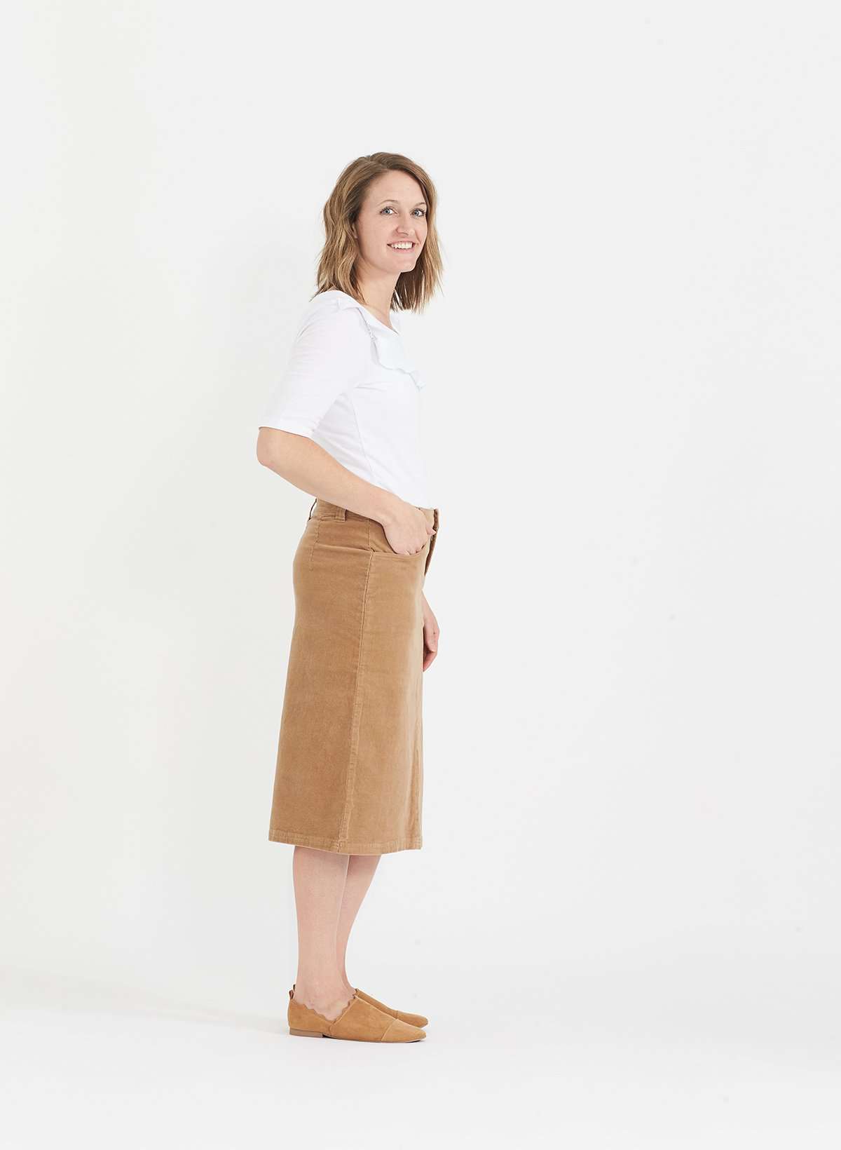Woman wearing a below the knee corduroy skirt. This skirt is a fin corduroy with a gold button snap, no slit and no back pockets. It comes in burgundy, teal, burnt orange and dark khaki.