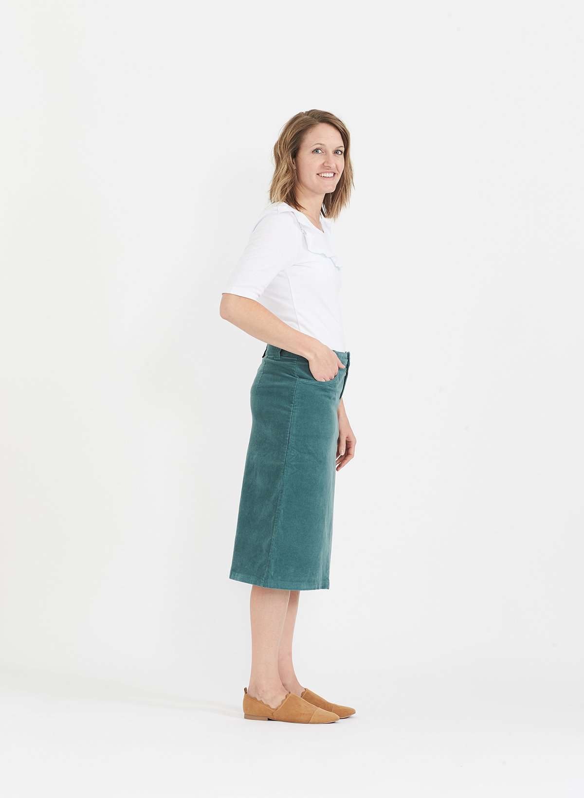 Woman wearing a below the knee corduroy skirt. This skirt is a fin corduroy with a gold button snap, no slit and no back pockets. It comes in burgundy, teal, burnt orange and dark khaki.