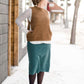 Woman wearing a below the knee corduroy skirt. This skirt is a fin corduroy with a gold button snap, no slit and no back pockets. It comes in burgundy, teal, burnt orange and dark khaki.