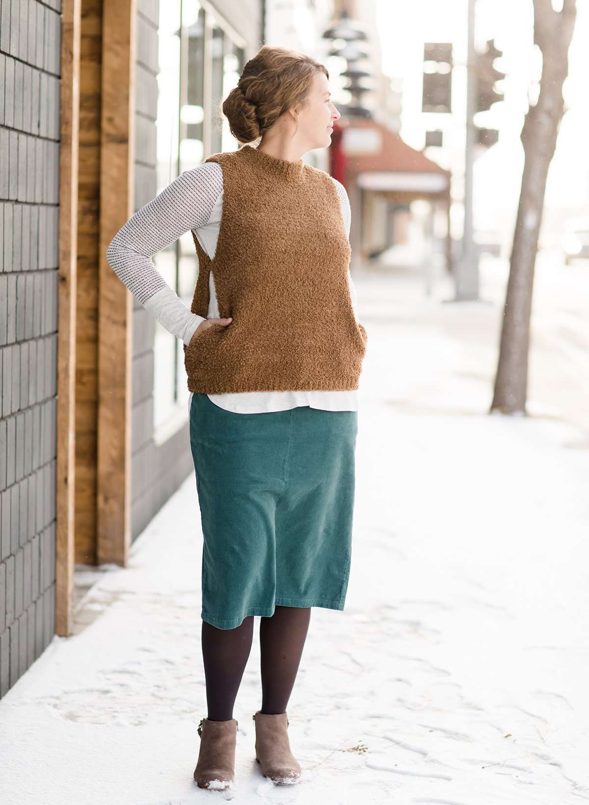 Woman wearing a below the knee corduroy skirt. This skirt is a fin corduroy with a gold button snap, no slit and no back pockets. It comes in burgundy, teal, burnt orange and dark khaki.