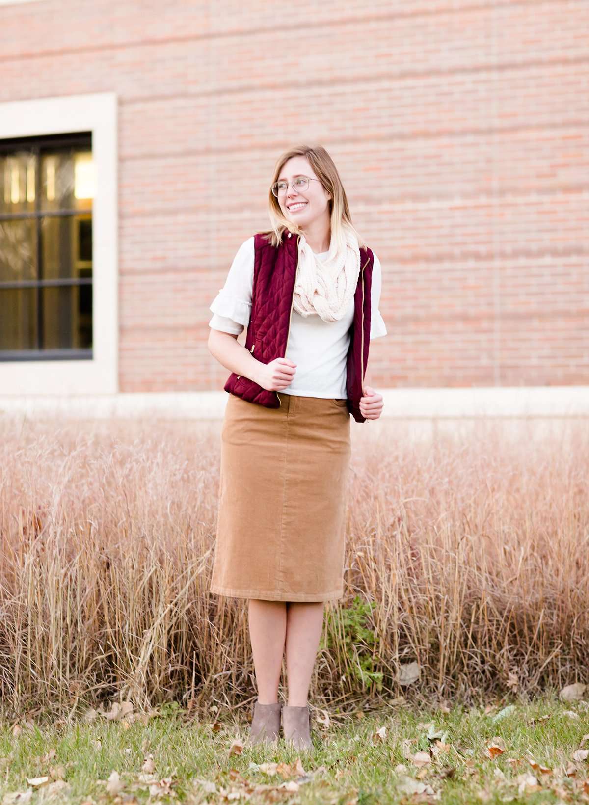 Woman wearing a below the knee corduroy skirt. This skirt is a fin corduroy with a gold button snap, no slit and no back pockets. It comes in burgundy, teal, burnt orange and dark khaki.