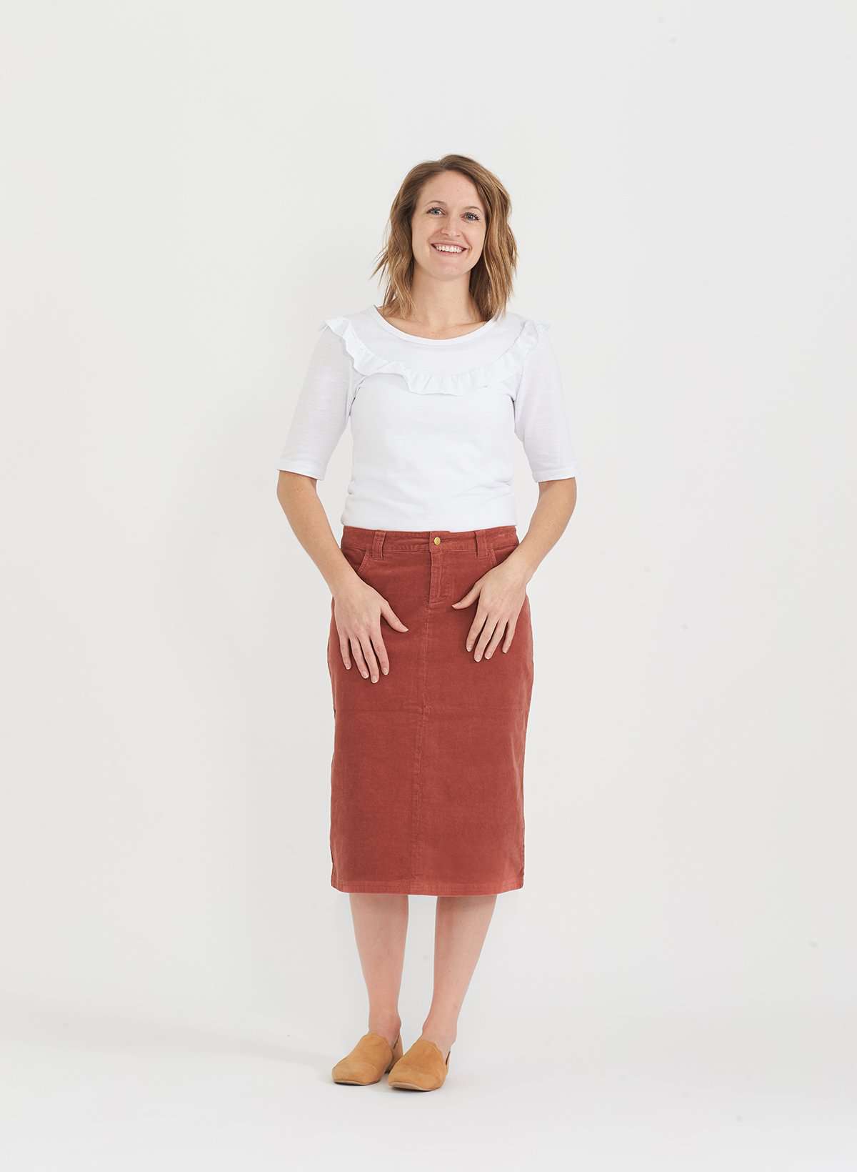 Woman wearing a below the knee corduroy skirt. This skirt is a fin corduroy with a gold button snap, no slit and no back pockets. It comes in burgundy, teal, burnt orange and dark khaki.