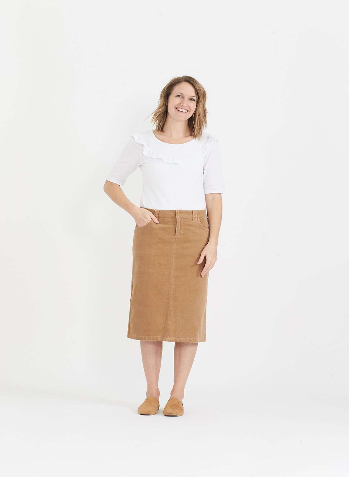 Woman wearing a below the knee corduroy skirt. This skirt is a fin corduroy with a gold button snap, no slit and no back pockets. It comes in burgundy, teal, burnt orange and dark khaki.