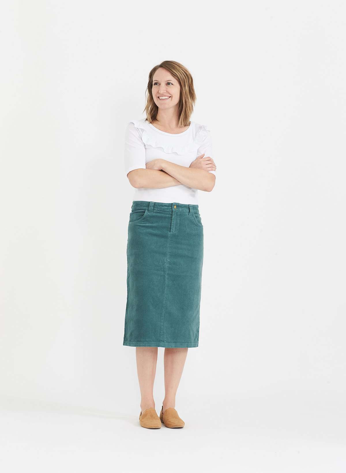 Woman wearing a below the knee corduroy skirt. This skirt is a fin corduroy with a gold button snap, no slit and no back pockets. It comes in burgundy, teal, burnt orange and dark khaki.