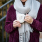 Woman wearing a gray fringe scarf that is super cozy and knit.