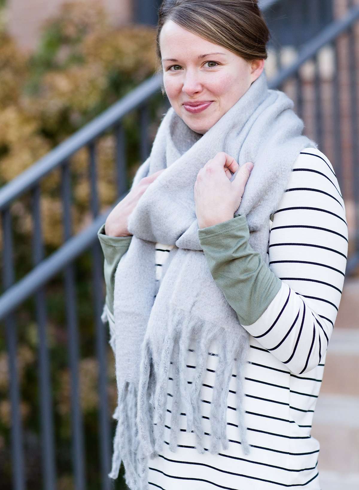 Woman wearing a gray fringe scarf that is super cozy and knit.