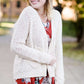 Young woman wearing a ivory chunky knit acrylic and wool sweater. This sweater has front pockets and features an open front.