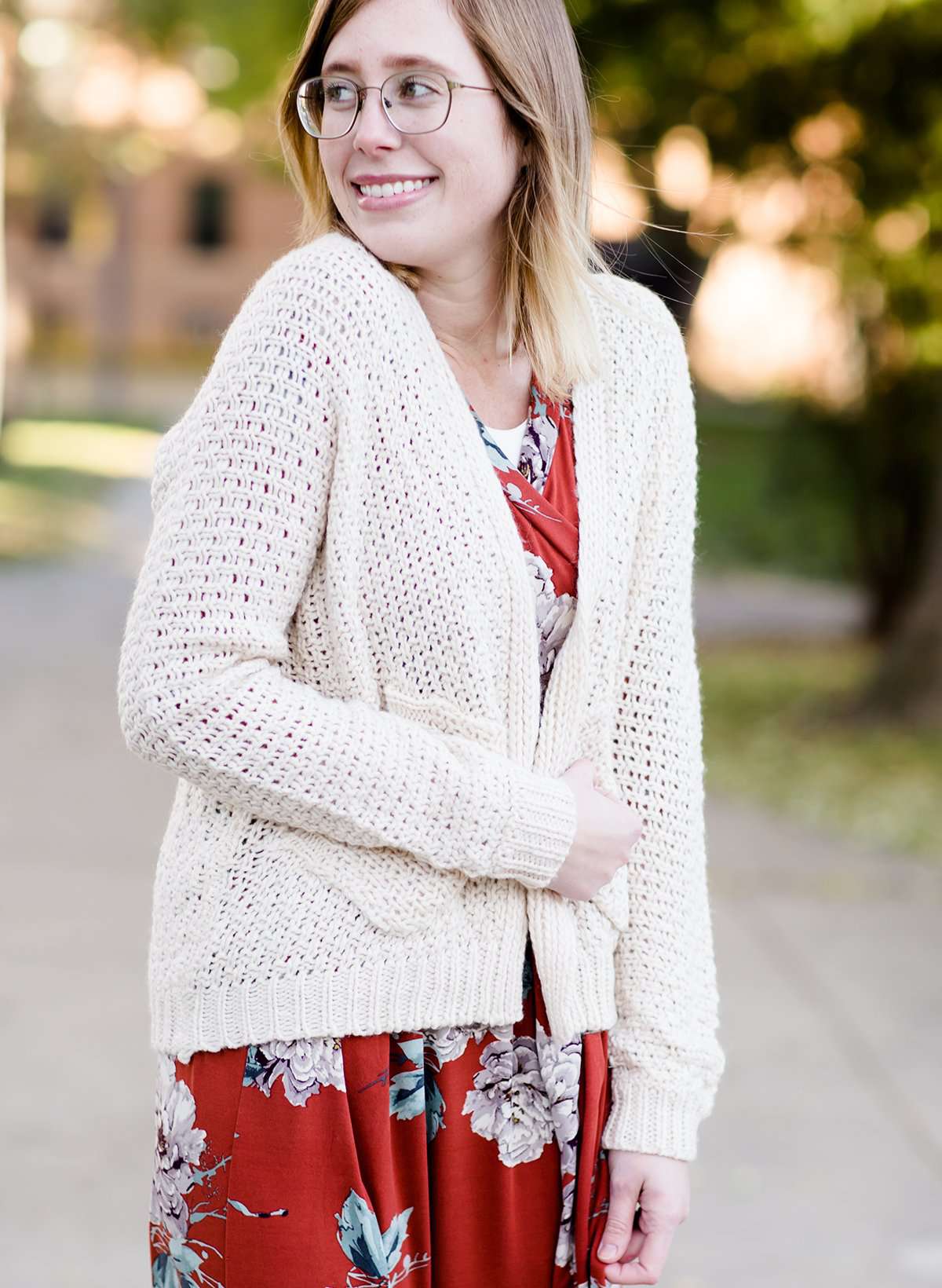 Young woman wearing a ivory chunky knit acrylic and wool sweater. This sweater has front pockets and features an open front.